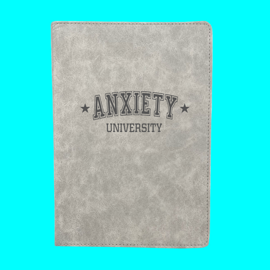 Gray notebook with 'ANXIETY UNIVERSITY' text on a turquoise background