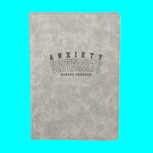 Gray notebook with 'Anxiety University Honors Program' text on a turquoise background